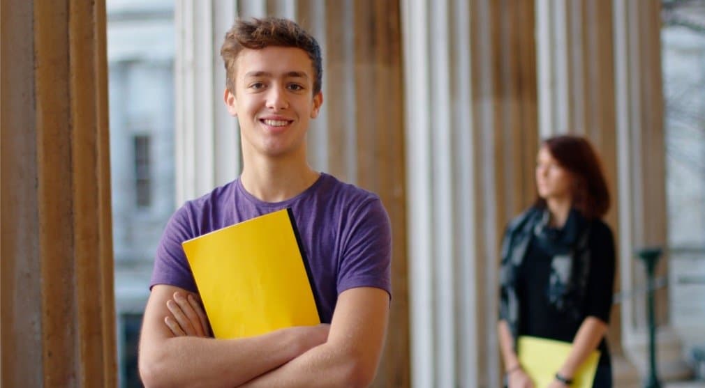 smiling-student-holding-yellow-folder-with-arms-closed-picture-id149344729